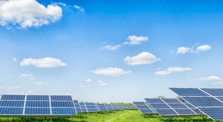 Solar panels in a green field under a clear blue sky, representing clean electricity and