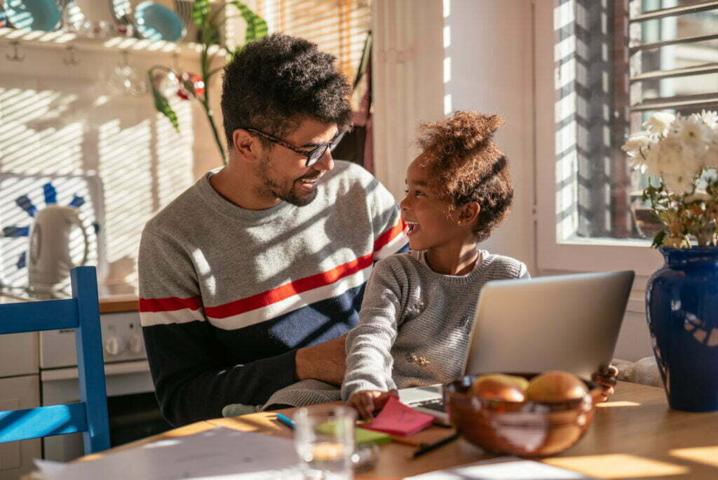 Father and daughter sharing a joyful moment at home, with a laptop and colorful stationery