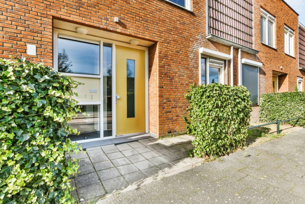 Stylish exterior door featuring a bright yellow color, surrounded by greenery, on a modern brick
