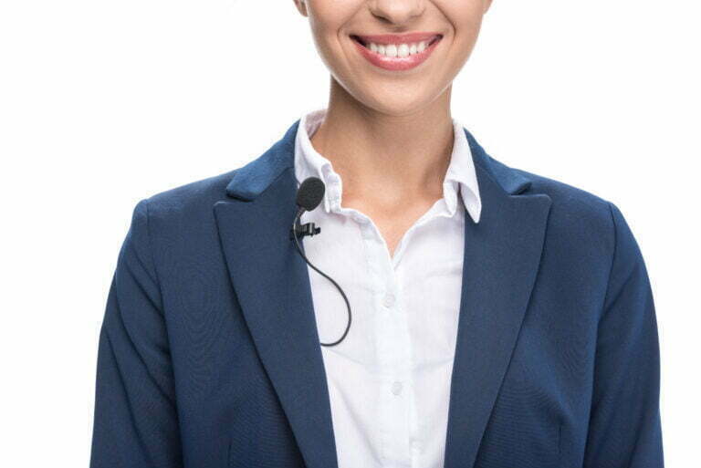 Smiling female newscaster wearing a suit and lavalier microphone, representing technology in media and audio