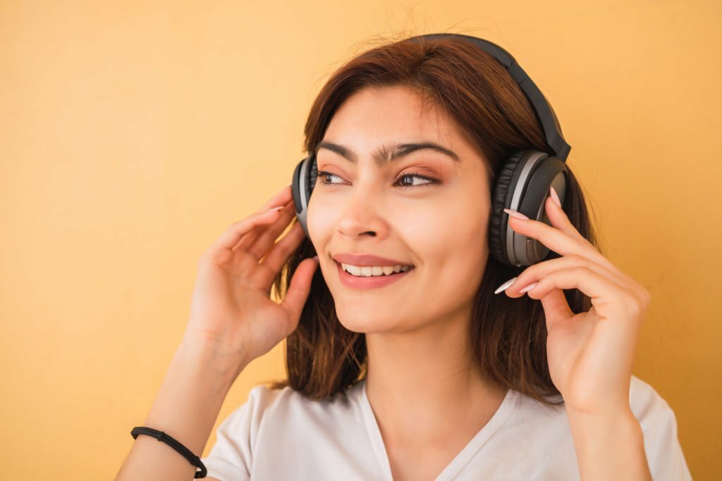 Young woman smiling while wearing headphones against a yellow background, illustrating enjoyment of music and